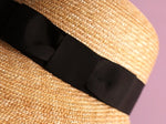 Load image into Gallery viewer, Close-up of a straw hat with a black grosgrain ribbon on a purple background　
